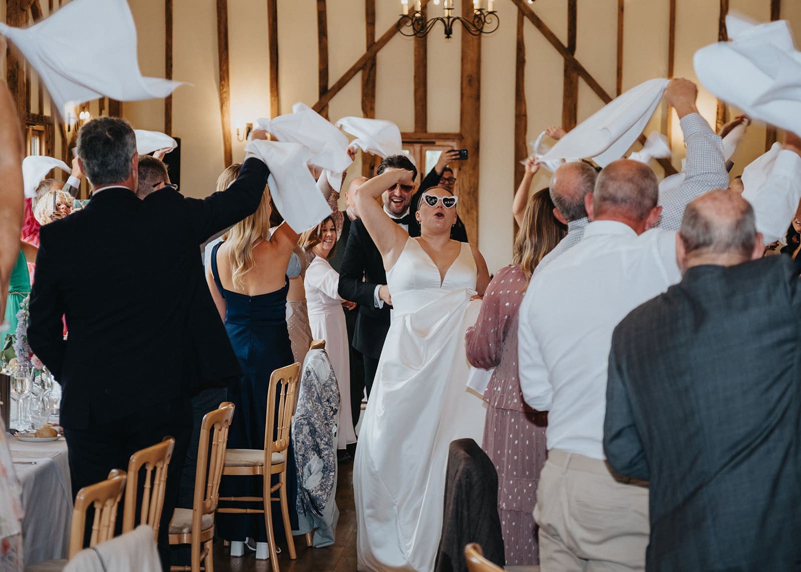Bride and groom entering their wedding reception as guests wave napkins, hosted by Liam Ball, Wedding Host in Essex.